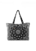 A black tote bag with a white paisley and floral bandana print, featuring dual shoulder straps and a front zippered pocket.