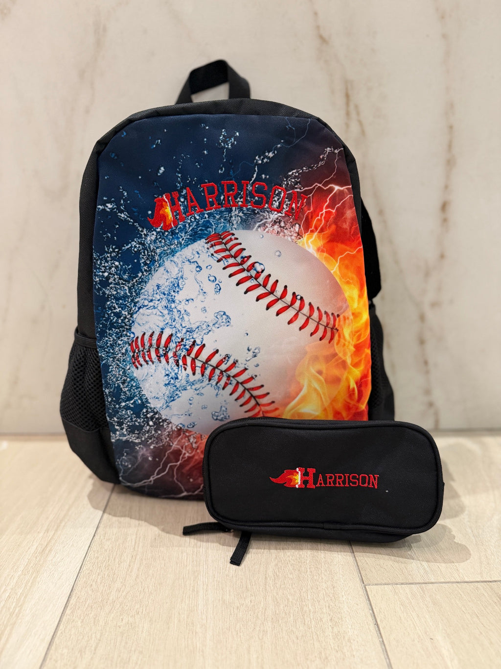 Fire and ice baseball backpack and black pencil case, each custom embroidered with the name Harrison in red varsity letters