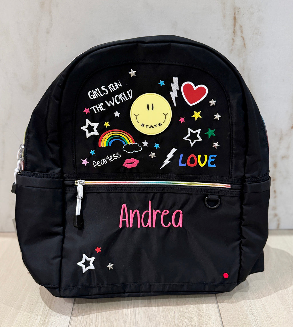 Black doodle print backpack with rainbows, hearts, and stars, custom embroidered with the name Andrea in pink script