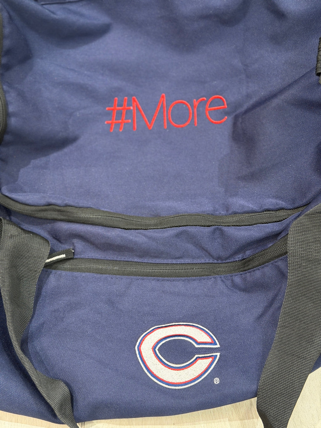 Navy duffel bag with #More custom embroidered in red above an embroidered team logo
