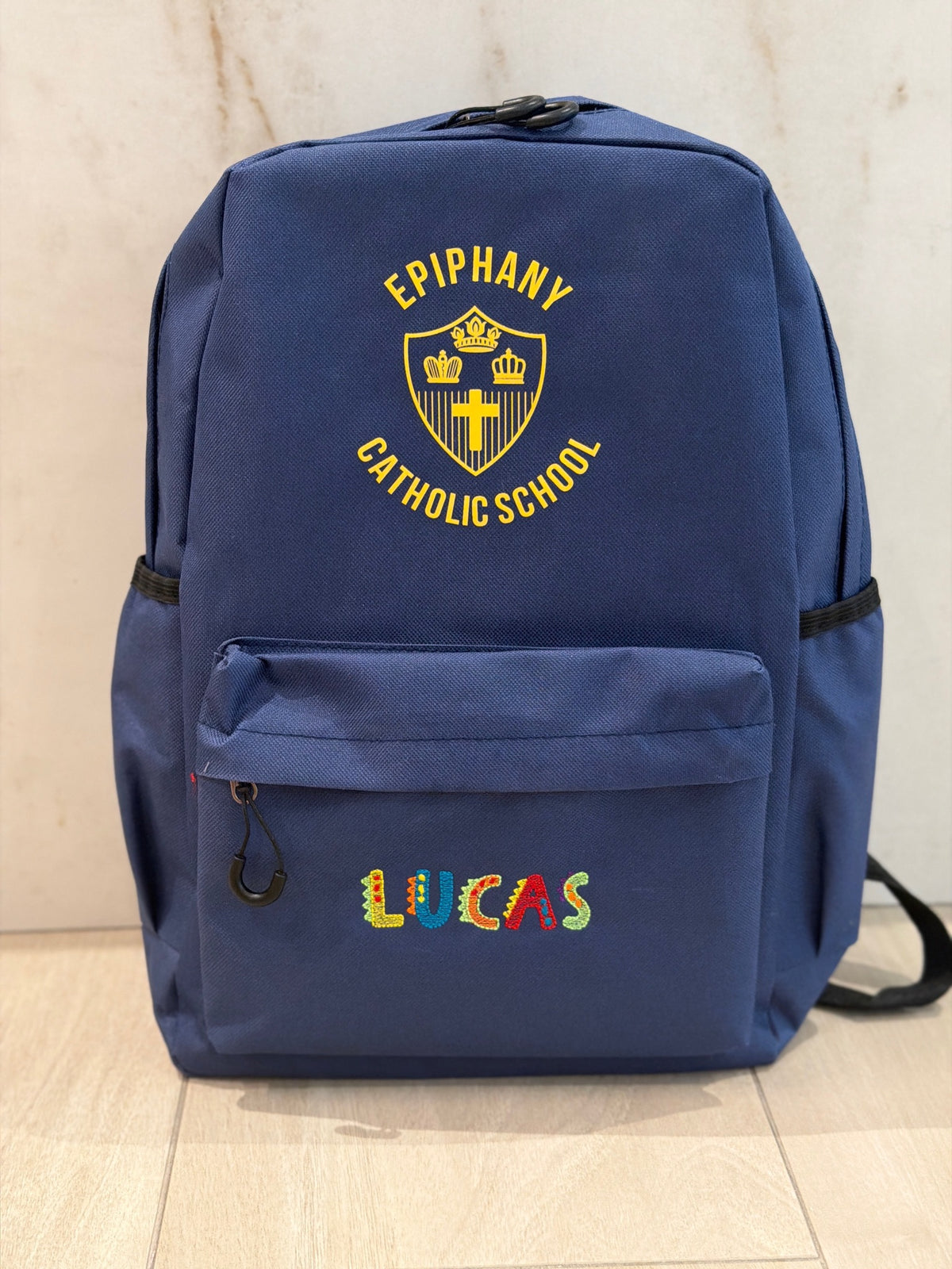 Navy school backpack with a gold school crest and the name Lucas custom embroidered in colorful dinosaur letters