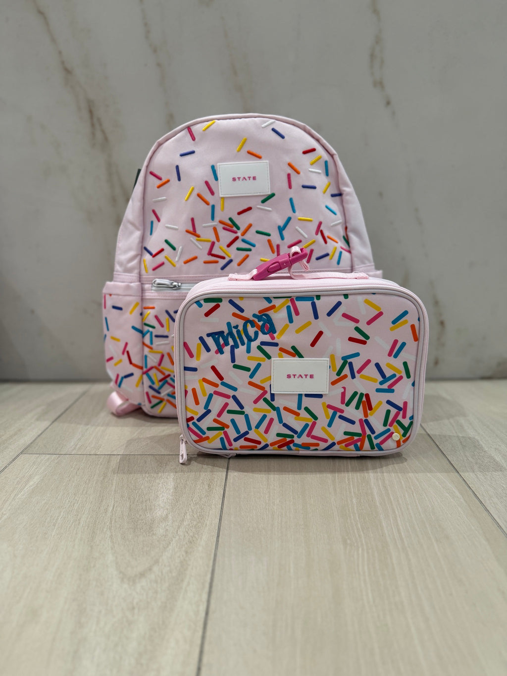 Pink rainbow sprinkles backpack and lunch box set with the name Mica custom embroidered in blue script